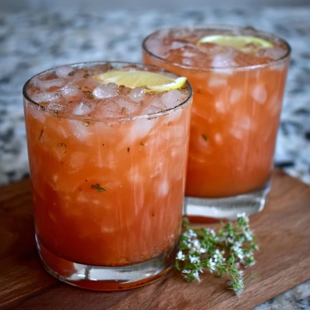 Close-up of a glass of fruit punch with floating fruit, ice cubes and a paper straw, bright red and refreshing